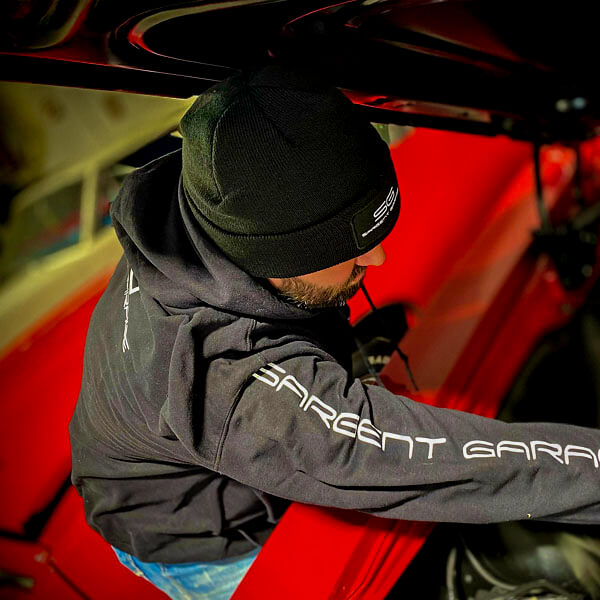 Man wearing Sargent Garage Pull-Over Hoodie Black leaning into an engine bay.