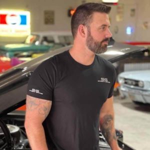 Man wearing black Sargent Garage T-Shirt standing next to a classic car.